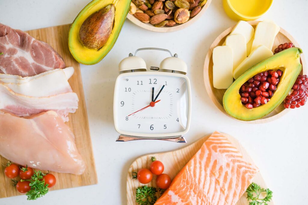 clock surrounded by raw proteins and avocado representing intermittent fasting