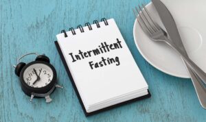 Understanding intermittent fasting with an image of a notepad with intermittent fasting written on it, a clock, and an empty dinner plate